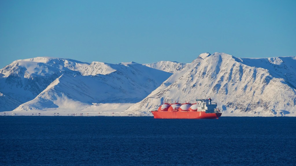Big red painted LNG (liquefied natural gas) carrier vessel lying at anchor in the arctic ocean in front of Sørøya island with snow-covered mountains near Hammerfest, Norway, Scandinavia in winter.
